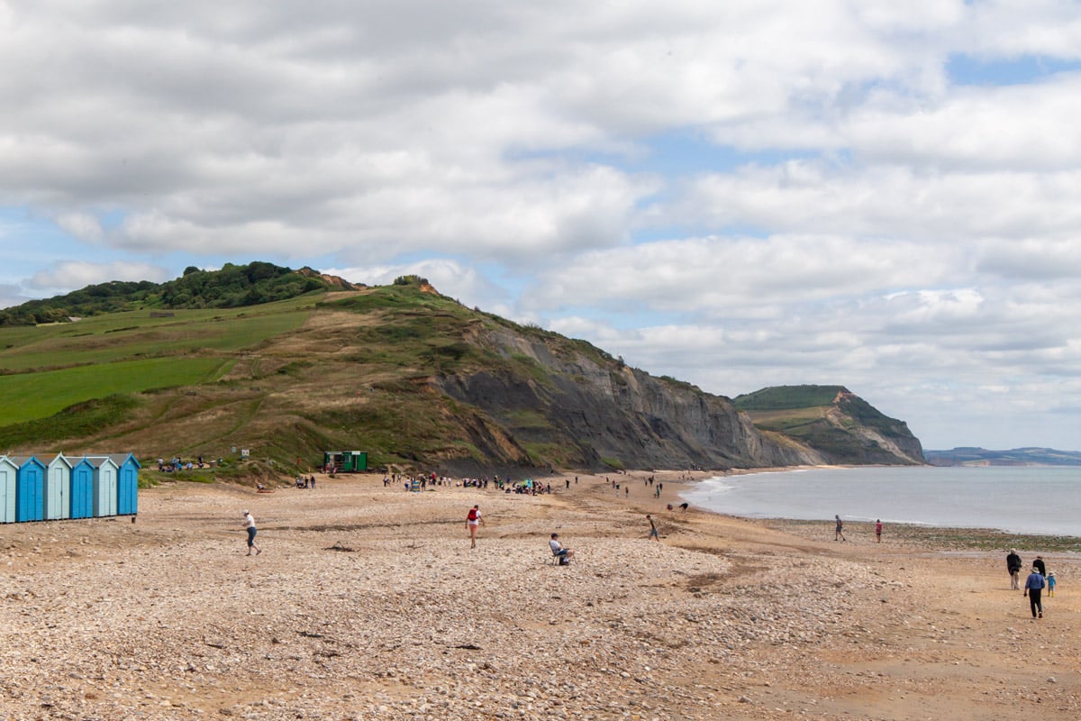 People hunt for fossils on the pebbly beach of charmouth under an overcast sky