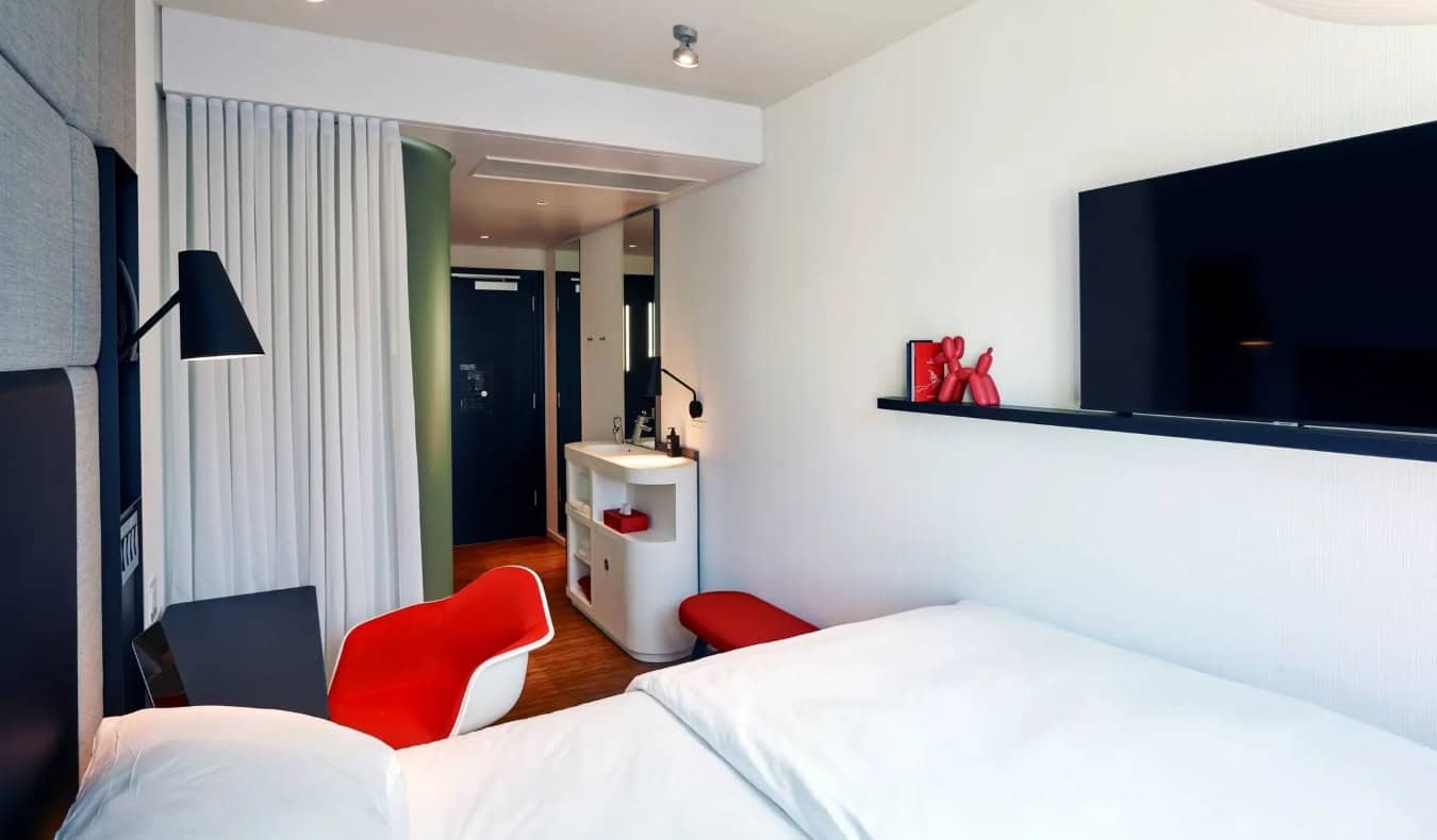 A compact hotel room with a bed, TV on the wall, and red furniture at the CitizenM Los Angeles hotel