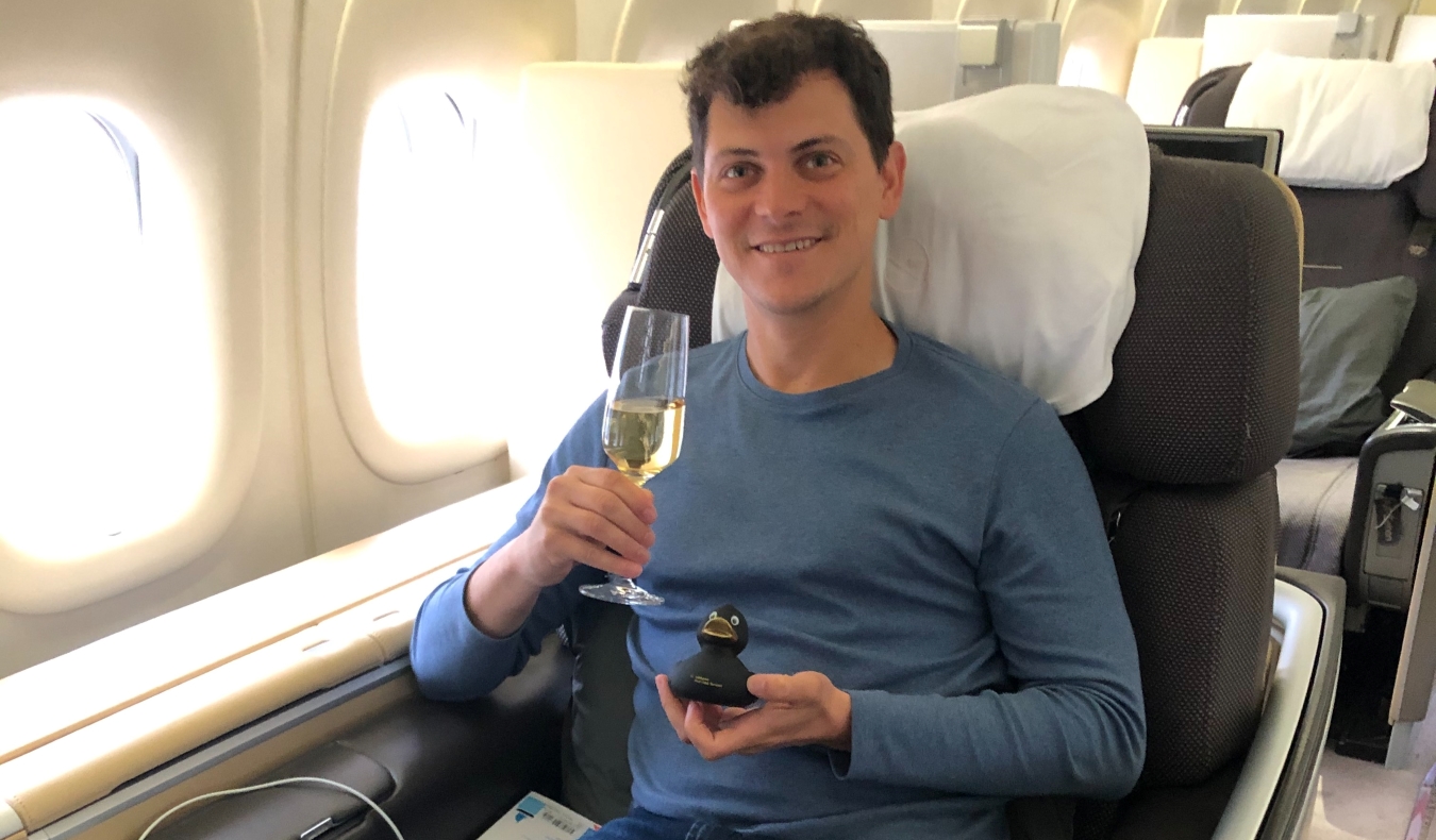 Nomadic Matt sitting in business class on a plane, holding up a glass of champagne