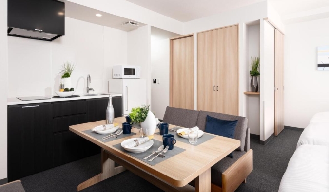 A kitchenette with a small sink, cooktop, counter, cabinets, and a wooden table in front at Mimaru Tokyo Ueno Okachimachi, an apartment hotel in Tokyo, Japan